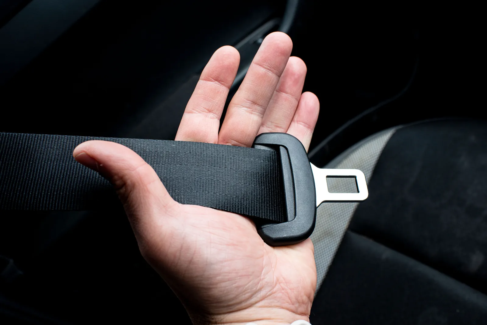 Hand holding a car seat belt latch, a reminder to get checked after a car accident