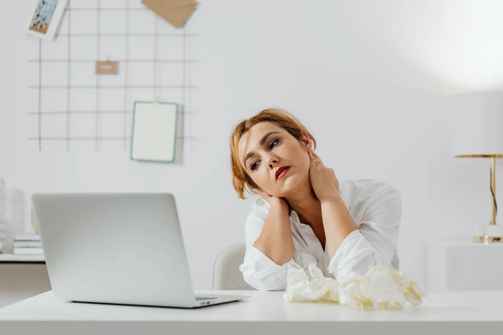Woman at a desk with a laptop, holding her neck in pain