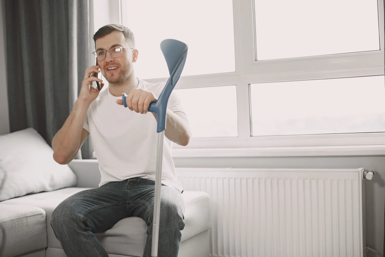 Man with a crutch resting on a sofa at home after a personal injury