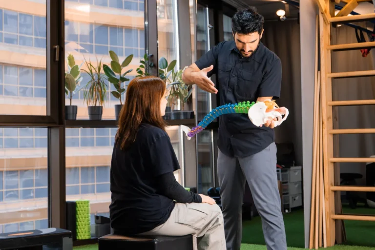 Practitioner explaining a spine model to a seated woman, the kind of model used to show degenerative disc changes