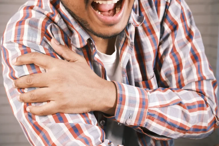 Man in a plaid shirt gripping his shoulder in pain